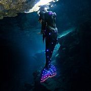 Mermaid with glowing purple lights in dark underwater cave.
