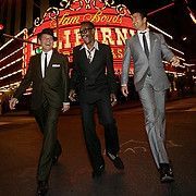 Men in suits walking in front of a casino sign, smiling and looking joyful; night setting.