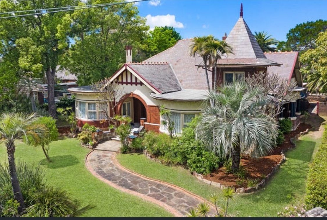 A small white house with a porch and bushes in front of it.