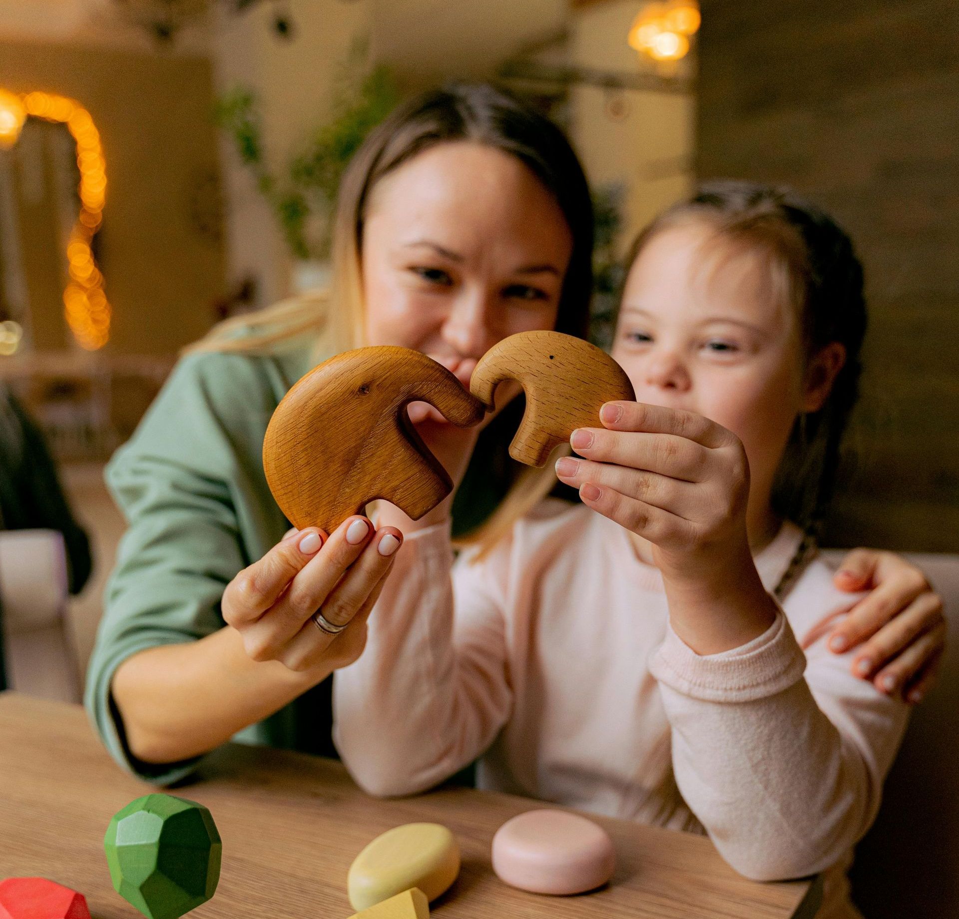 A woman and a little girl are sitting at a table holding a cookie in the shape of an elephant.