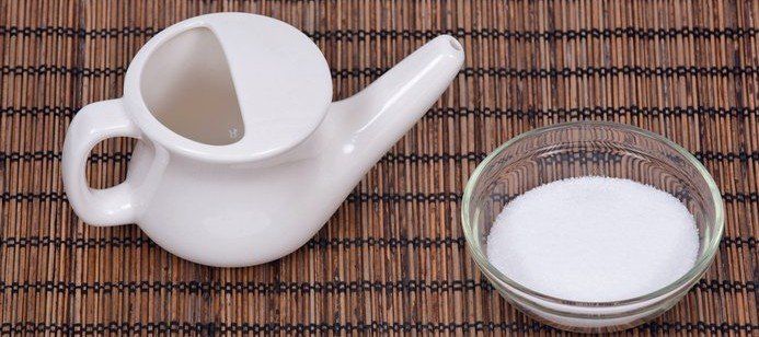 An image of a neti pot next to a small bowl of salt on a bamboo placemat