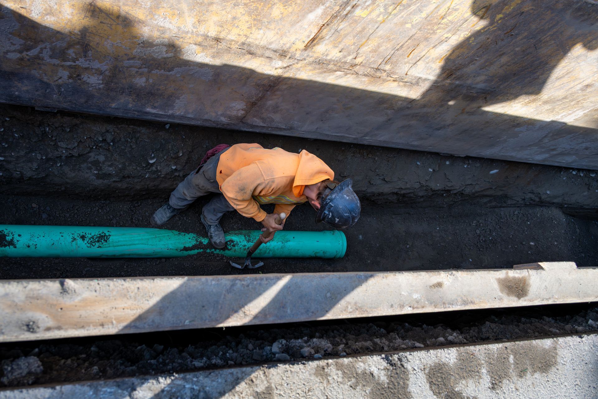 A worker is installing green pipe inside a narrow trench during a sewer line installation project