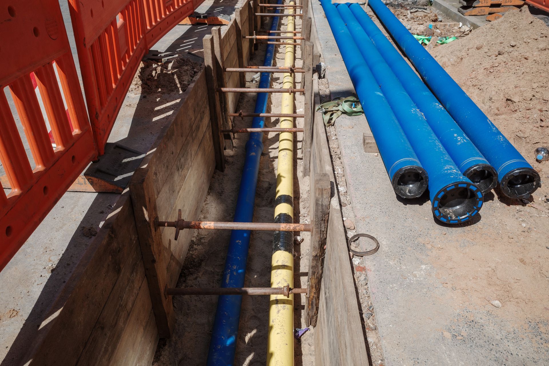 Construction site with blue and yellow pipes installed in a trench for utility work.