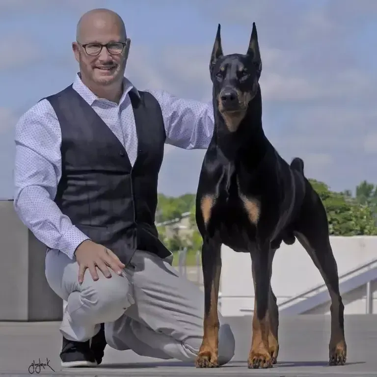 A man kneeling next to a large black dog