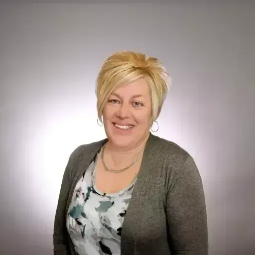 A woman wearing a gray cardigan and a floral shirt is smiling for the camera.