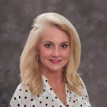 A woman in a white polka dot shirt is smiling for the camera.