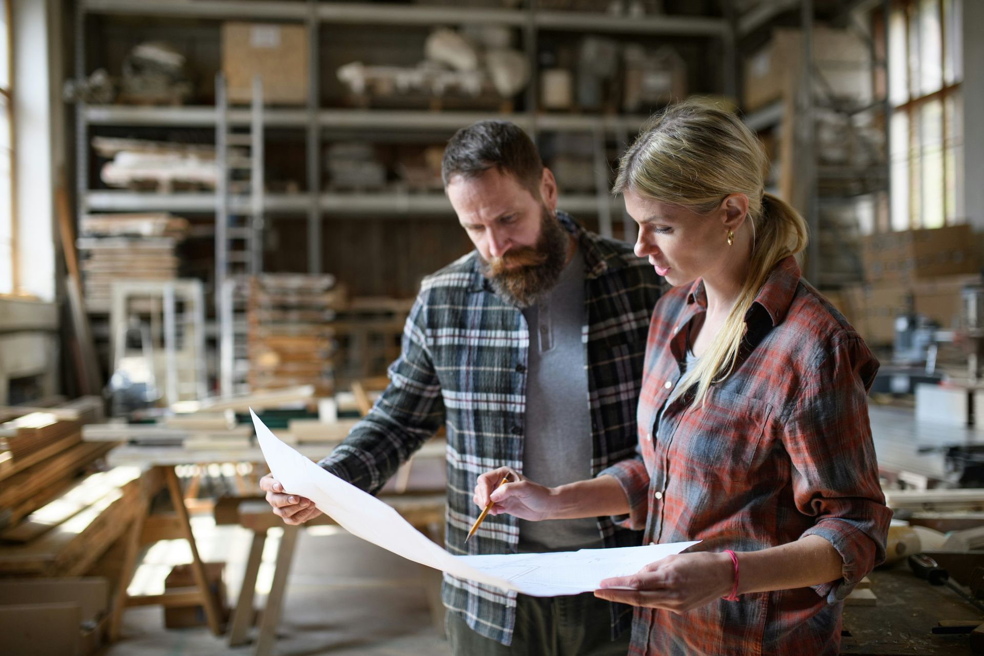 A man and a woman are looking at a piece of paper in a woodworking shop.