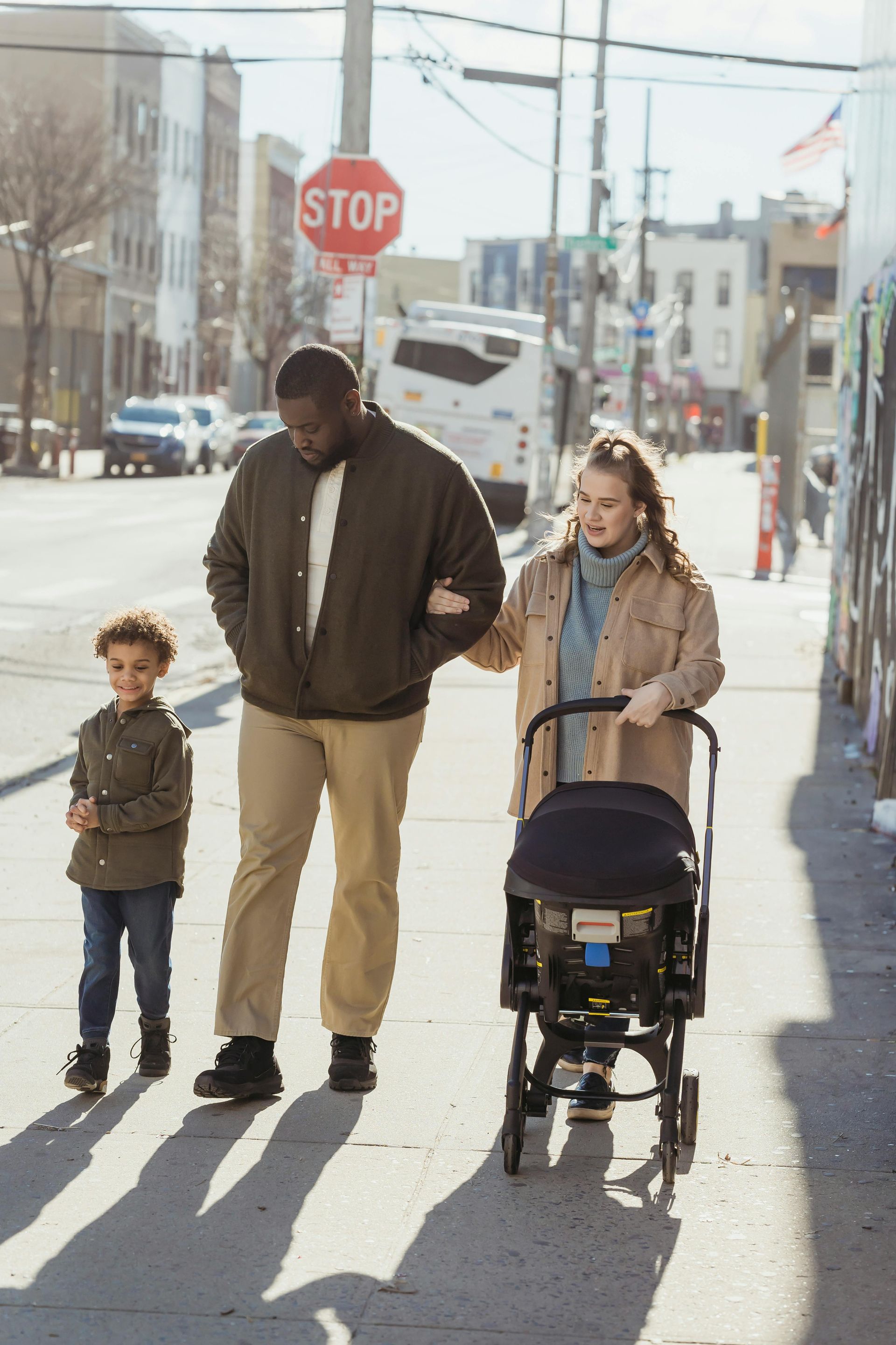 A man is pushing a stroller down a sidewalk with two children.