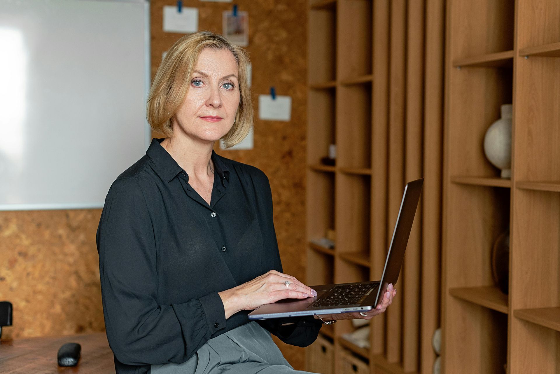 A woman is sitting at a table holding a laptop computer.
