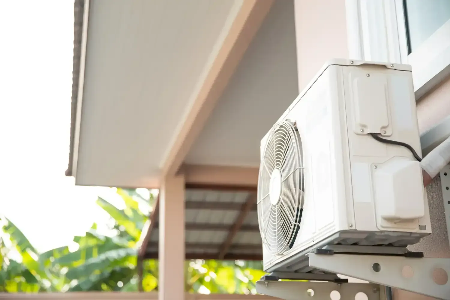 White air conditioner unit mounted on a light pink building exterior near a window.