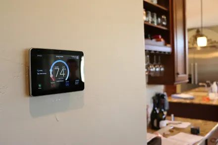 A smart thermostat displays 74 degrees on a wall in a kitchen.