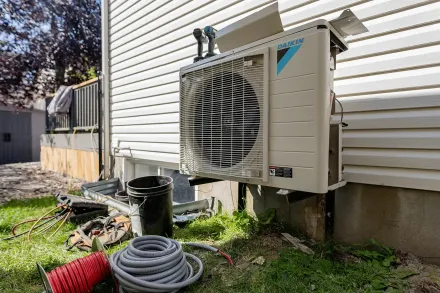 Outdoor Daikin HVAC unit installed on the side of a house, surrounded by tools and hoses.