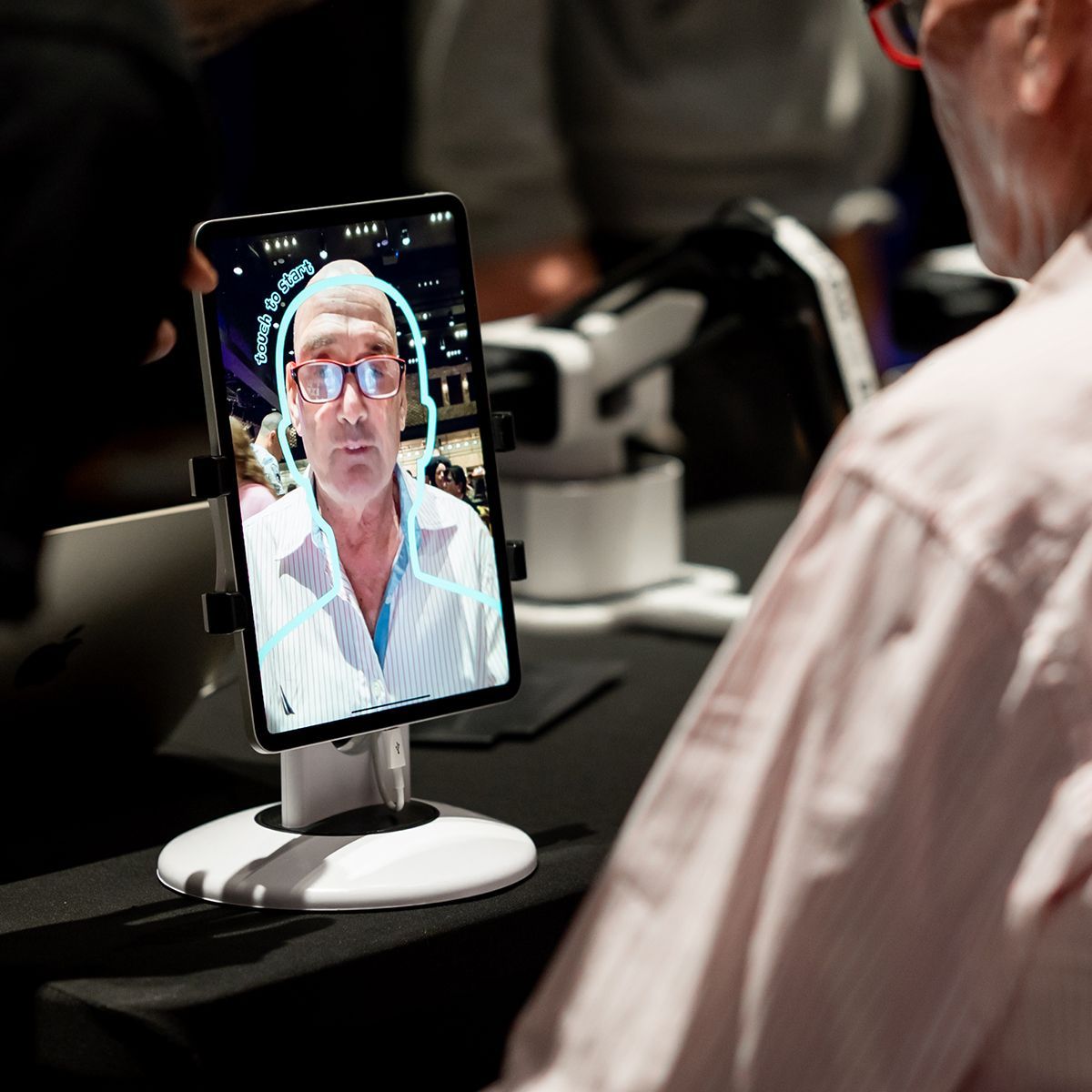 A person sits before a tablet on a stand, showing a real-time digital outline tracking the person's head and shoulders.