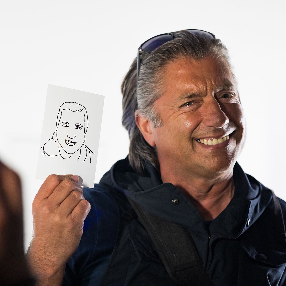 A smiling person holds a small, rectangular card featuring a simple line-drawing portrait of a person.