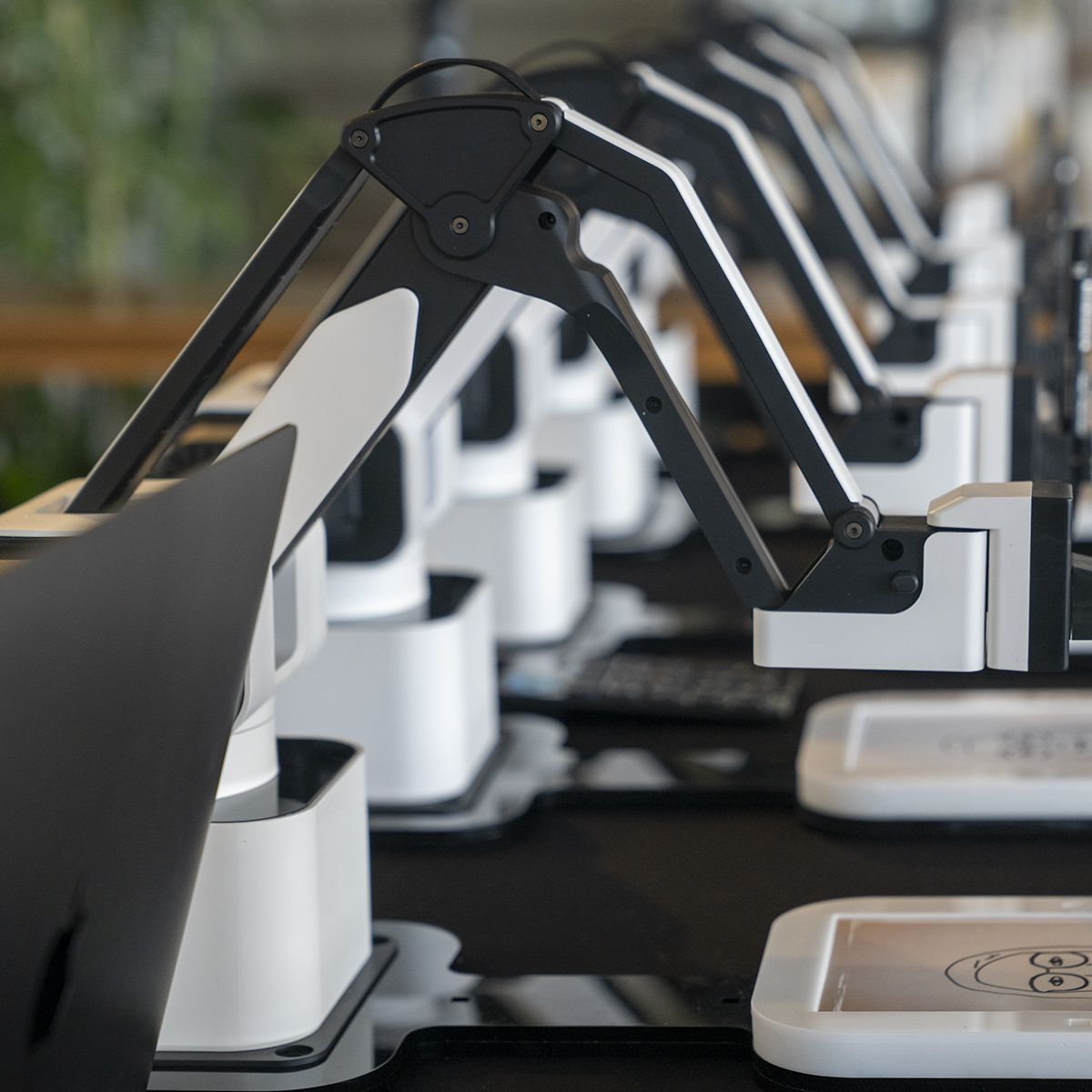 A row of robotic drawing arms in white and black, poised over individual tablets showing sketched faces.