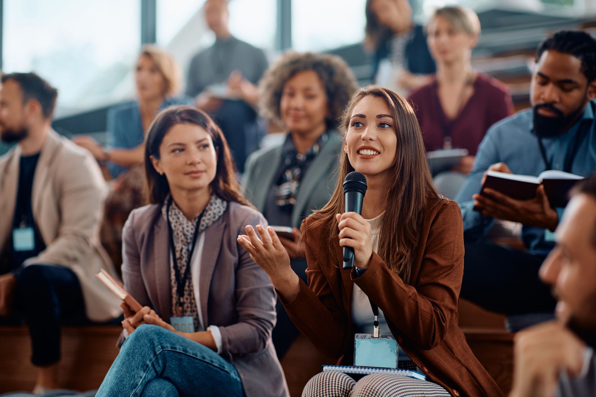 Woman speaking into a microphone during a conference. She gestures with her hand as attendees watch.