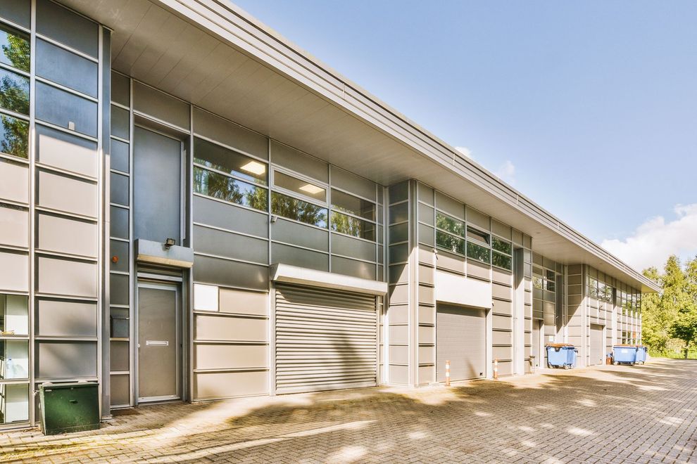 Modern commercial building with gray siding, large windows, and roll-up doors, on a sunny day.