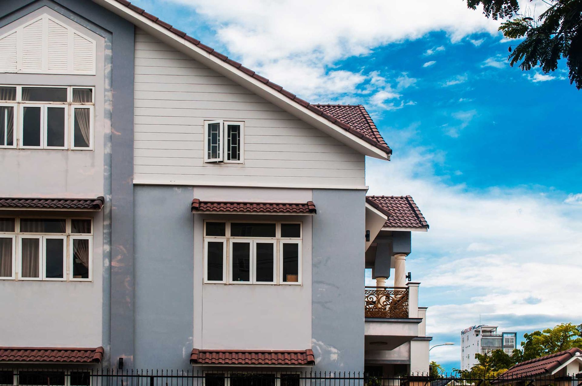 Two-story house with blue and white exterior against a partly cloudy sky. Brown roof and window awnings.