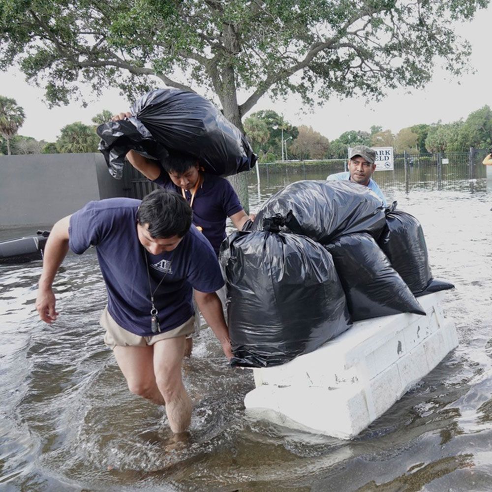 Two men are carrying bags of trash through a flooded area