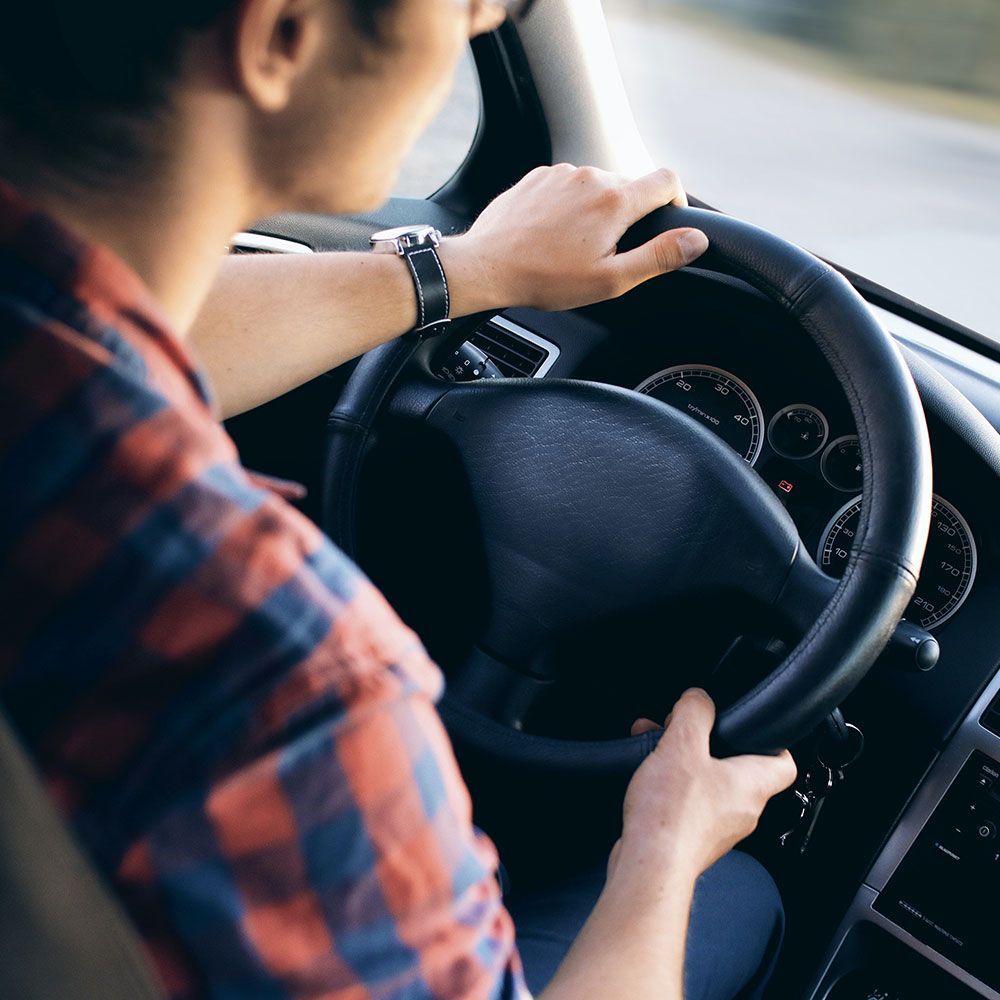 A man in a plaid shirt is driving a car