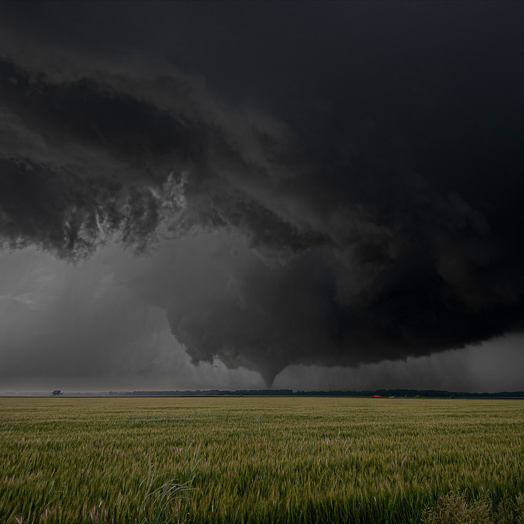 A large tornado is moving through a grassy field.