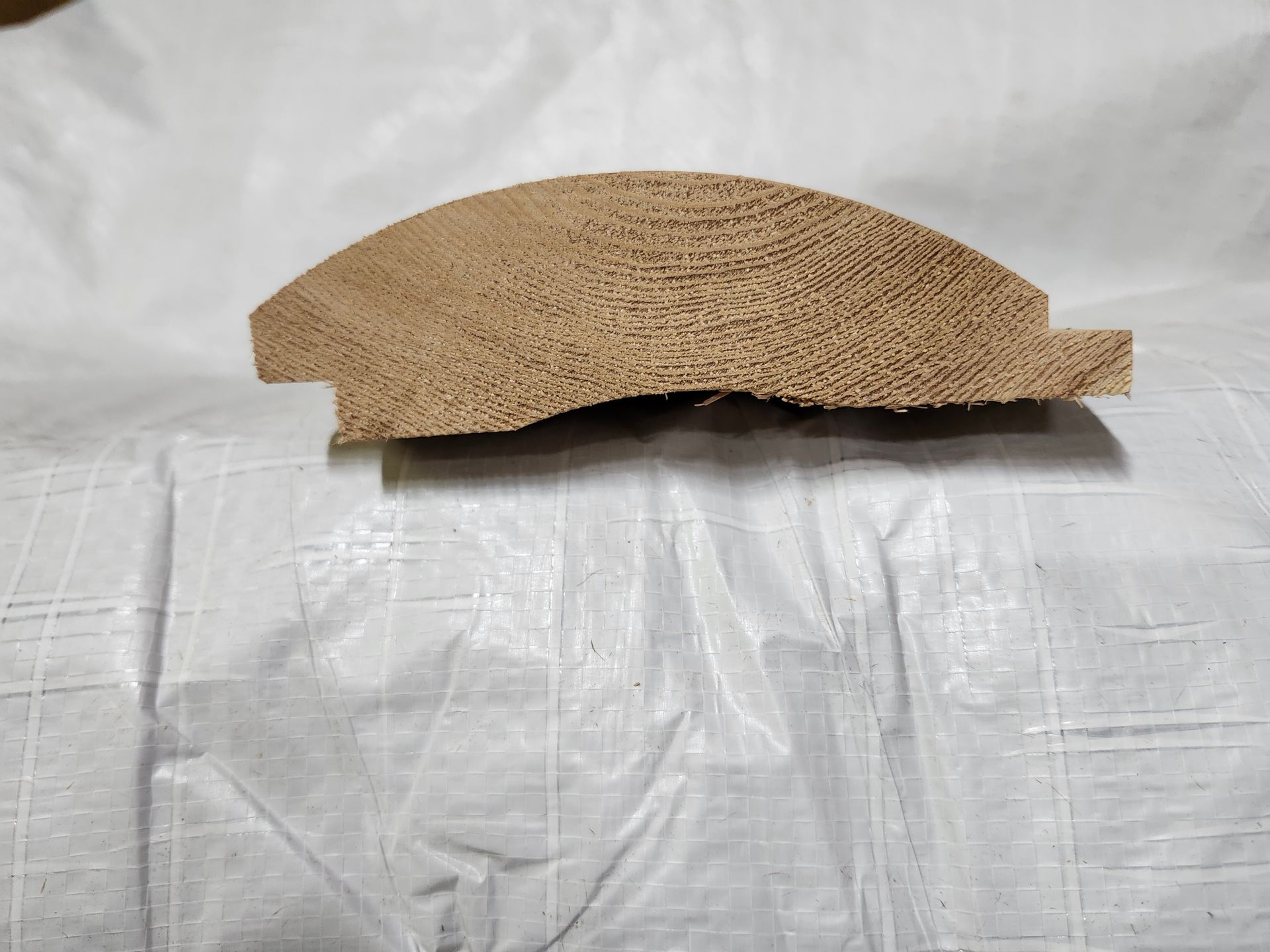 Cross-section of wood molding, showcasing curved top and a small ledge, with visible wood grain.