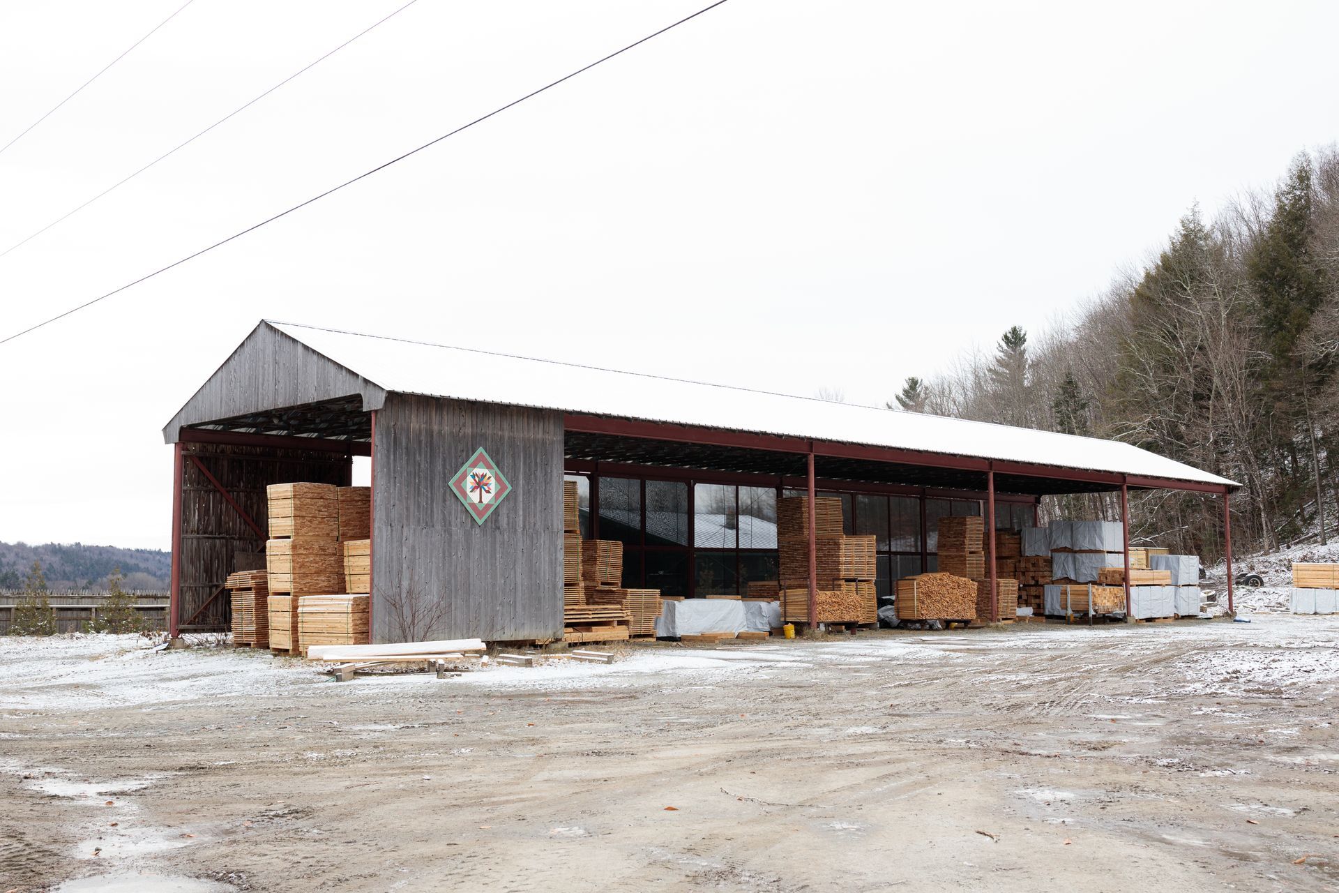 A wooden lumber storage shed with stacks of lumber, in a snowy outdoor setting.