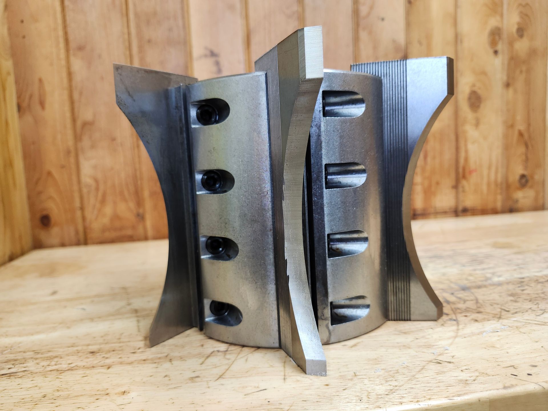 Large metal industrial tool with curved blades and bolt holes on a wooden surface.