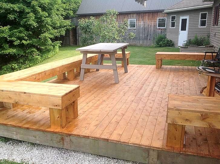 Wooden deck with built-in benches, table, and surrounding yard.