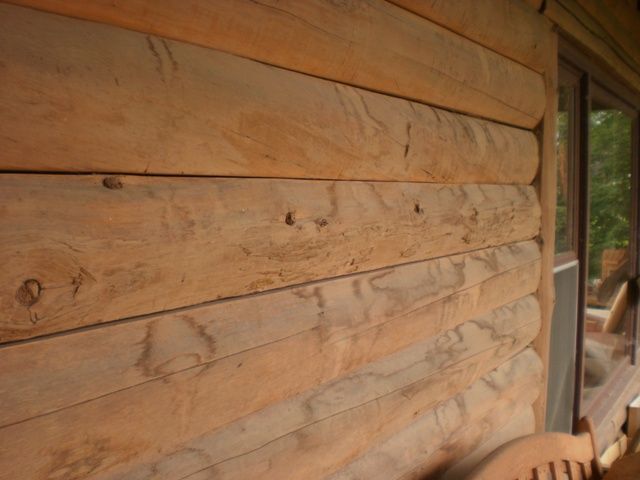 Wooden log cabin exterior wall, light brown, with window visible on right side.