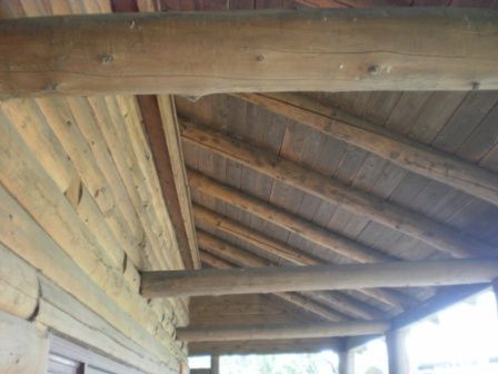 Wooden porch ceiling with log beams, horizontal siding, and angled wood boards.