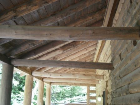 Wooden porch roof with logs and beams supporting it.