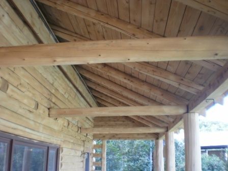 Wooden log cabin porch with exposed beams and rafters.