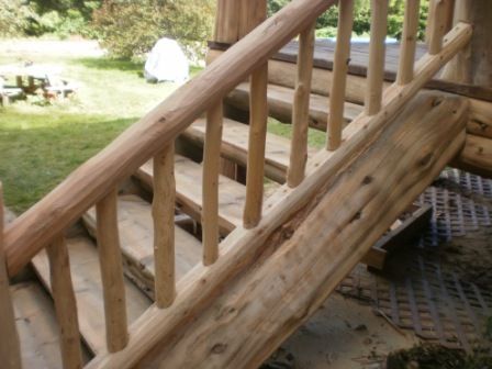 Wooden log stairs with a handrail on the left, and a wooden ramp on the right, outdoor setting.