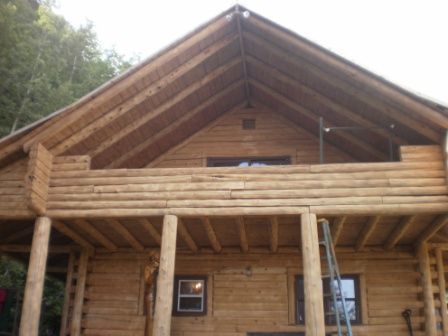 Log cabin exterior with porch, second-story balcony, and a gabled roof.