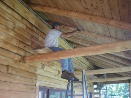 Man on ladder hammering wood beams in a wooden structure.