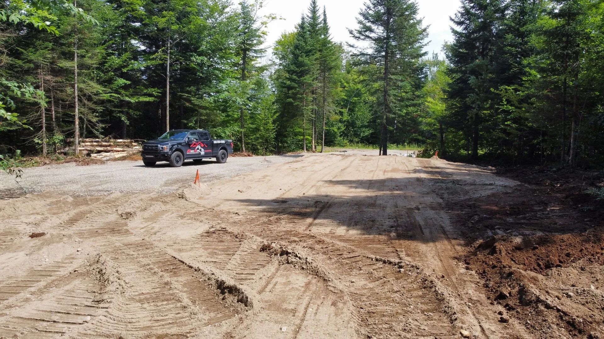 Une camionnette noire garée sur une dalle de gravier dans une zone boisée dégagée, sous un ciel lumineux.