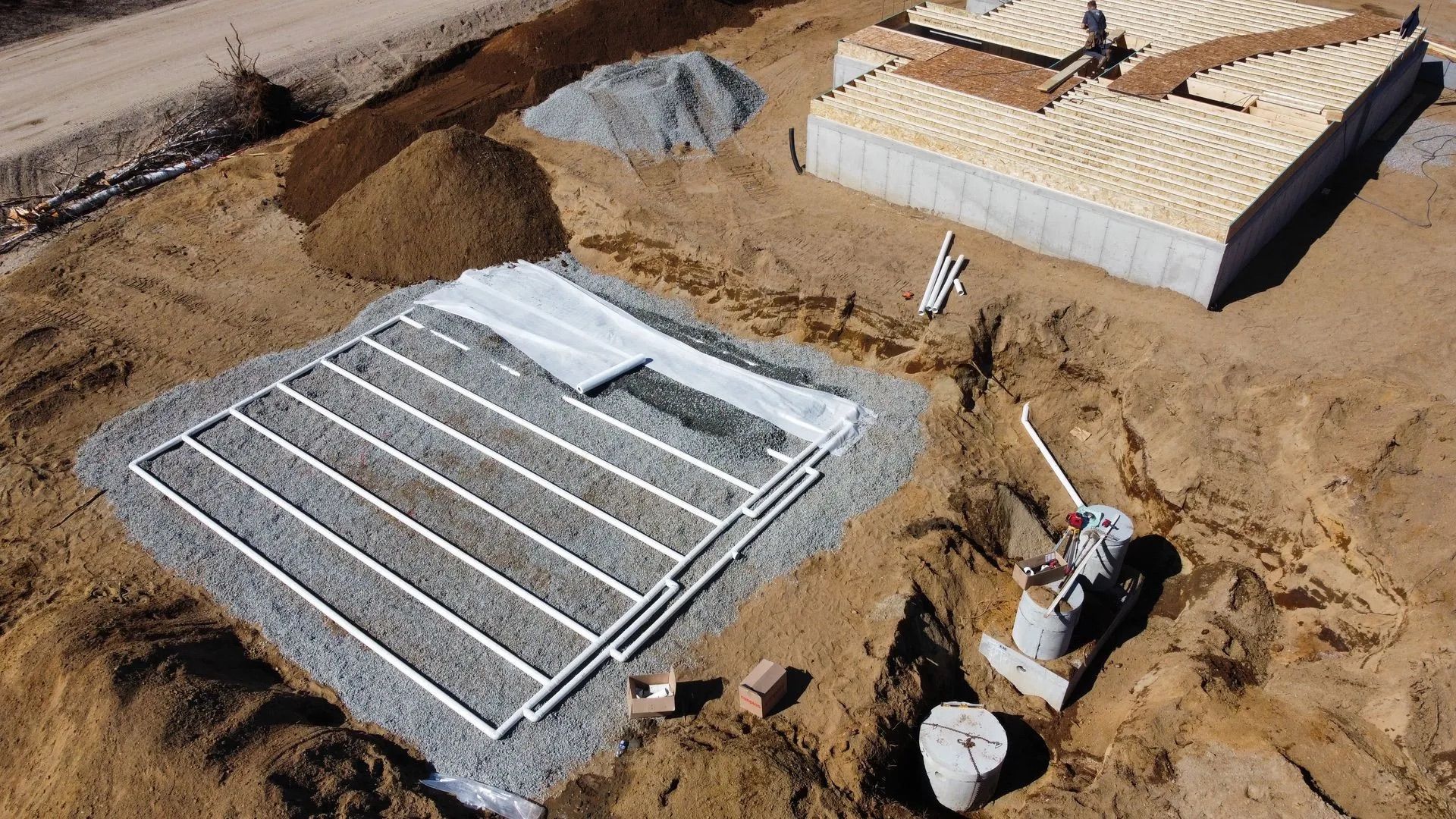 Vue aérienne d'un chantier de construction montrant un champ d'épandage septique rempli de gravier avec des canalisations et une fondation en béton.