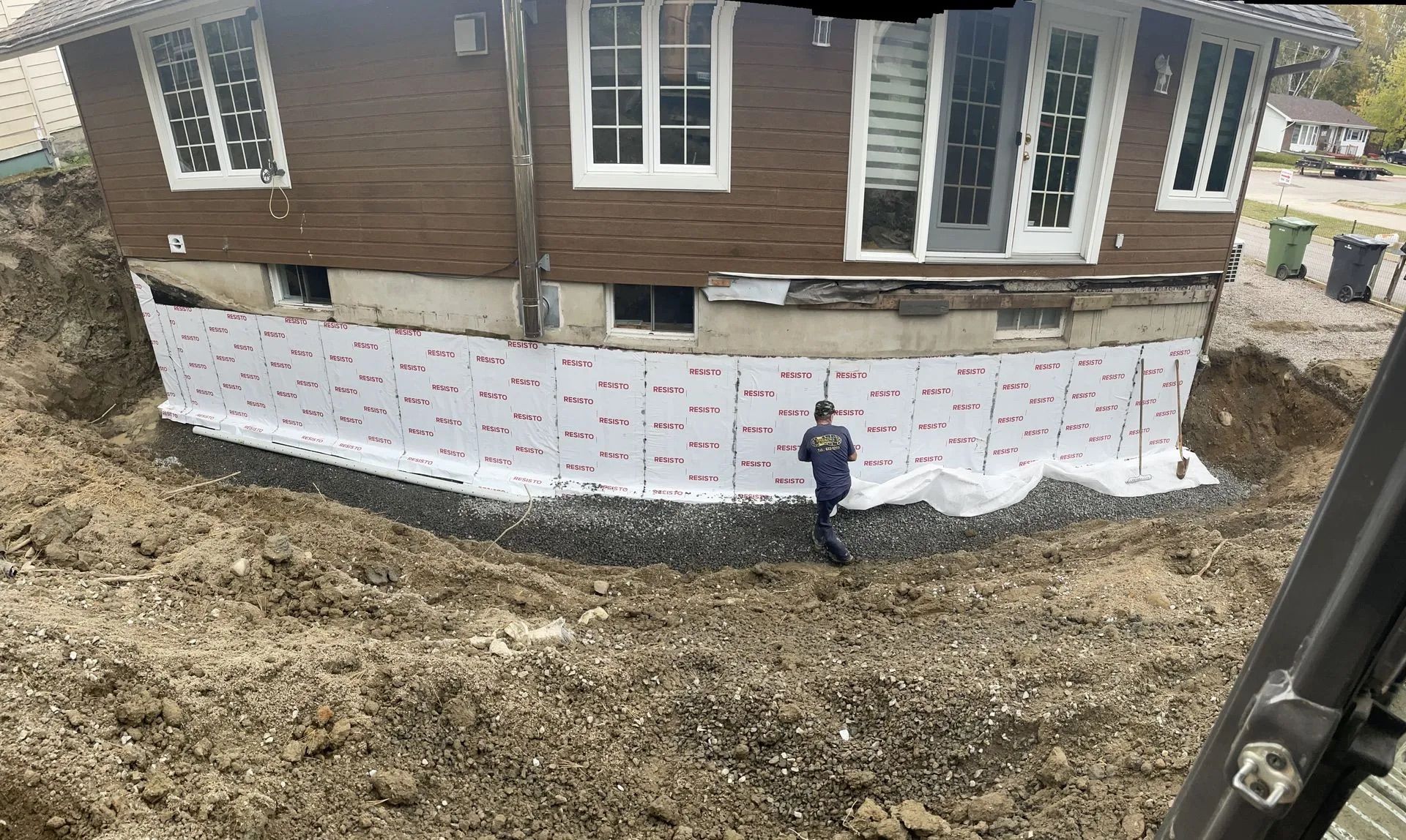 Une personne se tient à côté des fondations d'une maison recouvertes de panneaux isolants blancs lors de travaux d'excavation en extérieur.