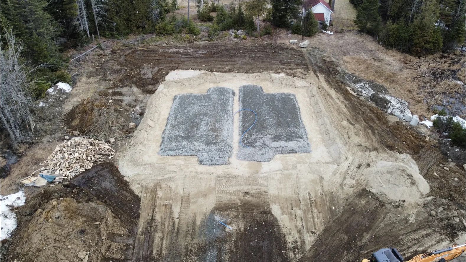 Vue aérienne d'un chantier de construction montrant deux semelles de fondation rectangulaires remplies de gravier, installées dans un sol défriché.