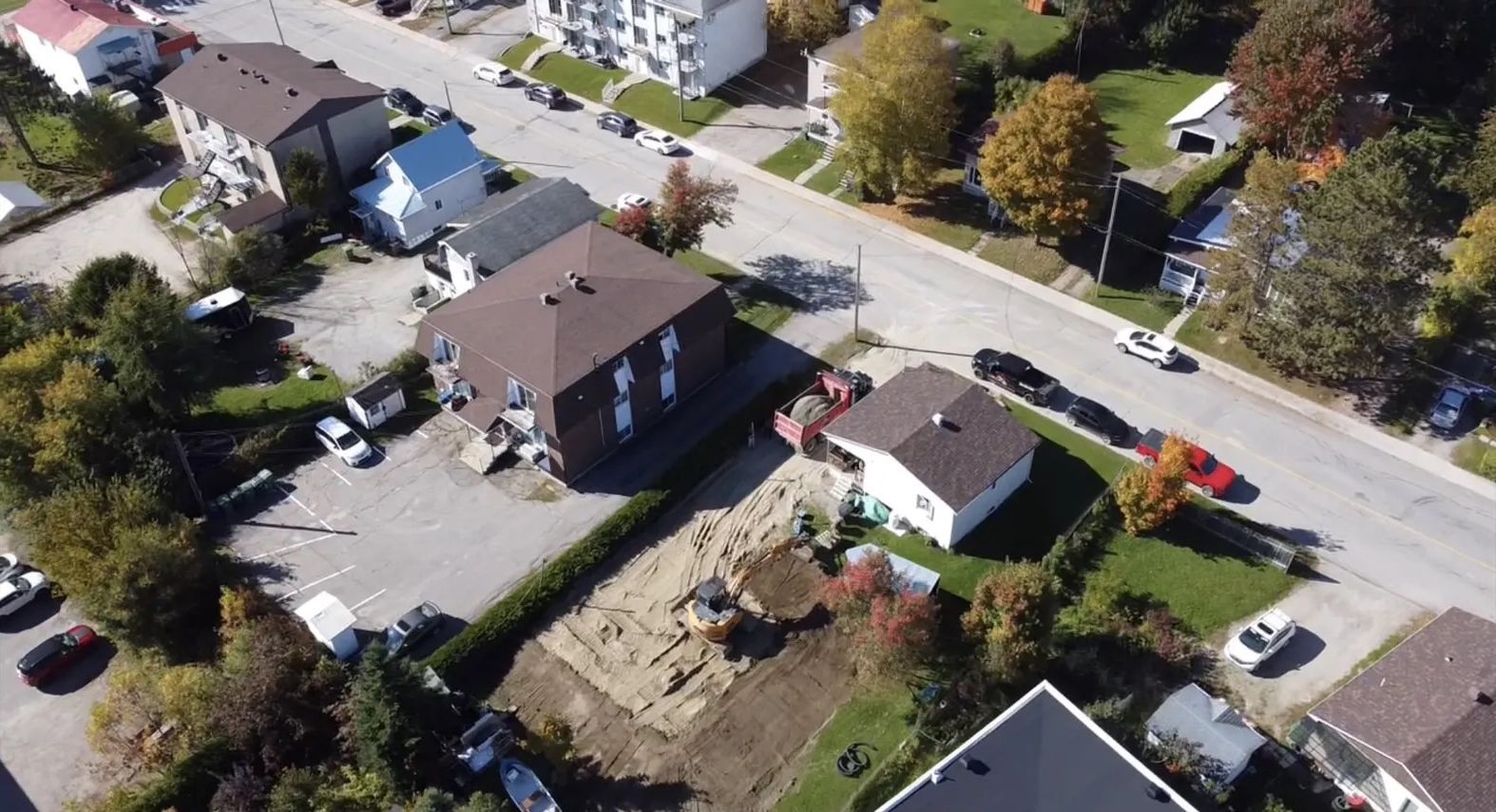 Vue aérienne d'un quartier résidentiel avec plusieurs maisons, des allées pavées, un chantier de construction et des tramways.