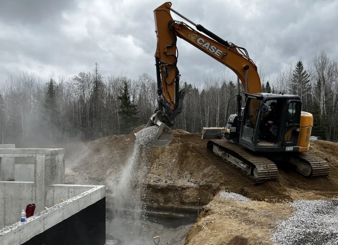 Une pelle mécanique Case jaune déverse du gravier dans une fondation en béton sur un chantier de construction.
