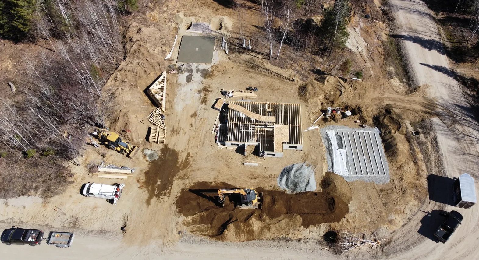 Vue aérienne d'un chantier de construction rural avec des fondations en béton, des engins lourds et des matériaux de construction.
