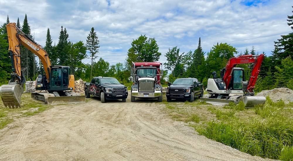 Une scène de chantier montrant une excavatrice orange, deux camionnettes noires, un camion-benne et une mini-excavatrice rouge.