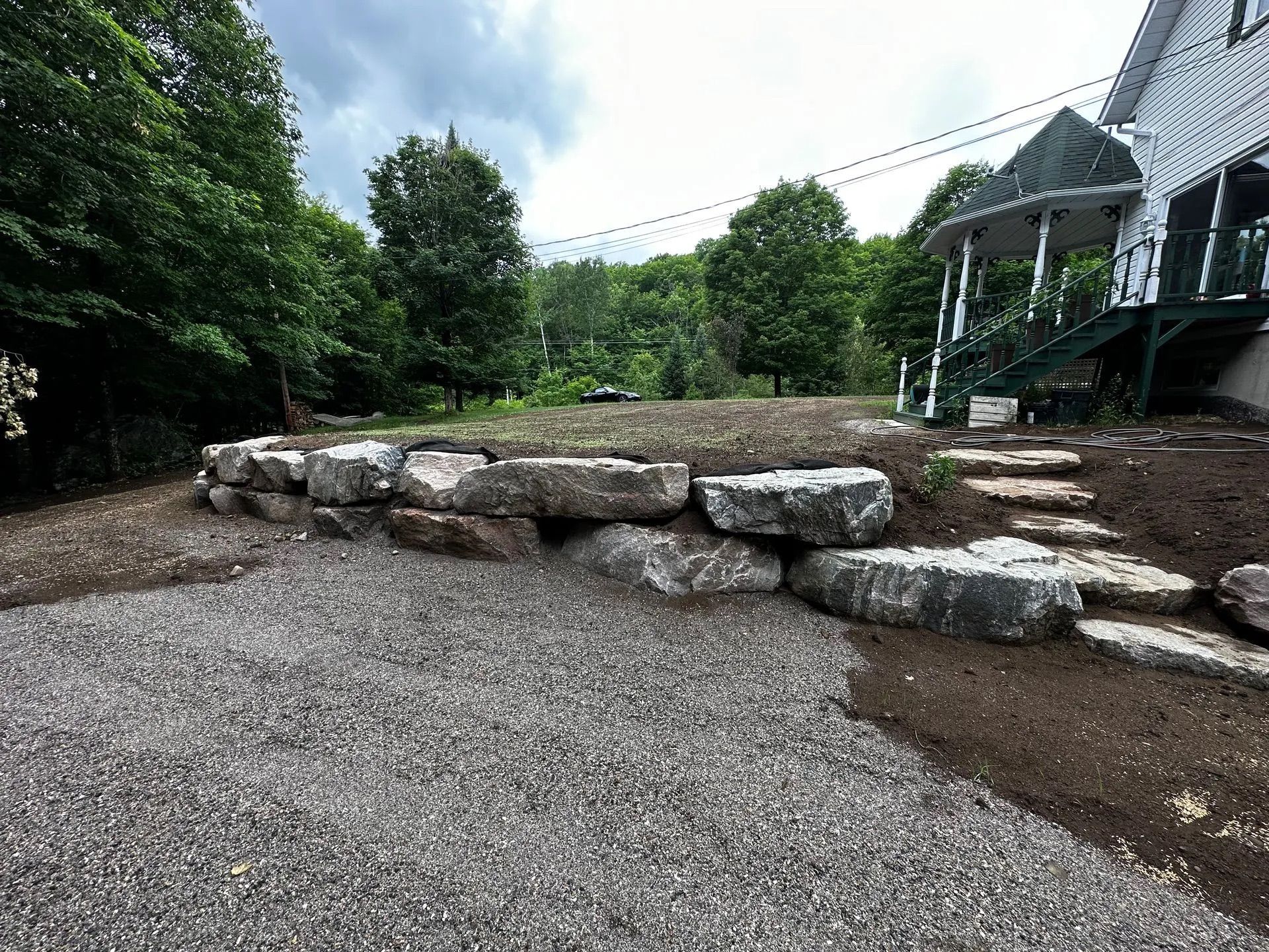 Un paysage caractérisé par un grand mur de soutènement en pierre, une allée de gravier et un escalier en pierre menant au porche d'une maison.