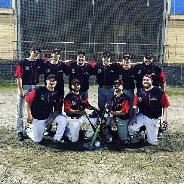 Une équipe de baseball pose sur un terrain ; cinq joueurs se tiennent debout derrière quatre coéquipiers agenouillés, tous vêtus d'uniformes d'équipe assortis.