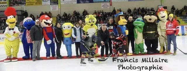 Une rangée de mascottes costumées et de personnes posant pour une photo de groupe sur une patinoire intérieure.