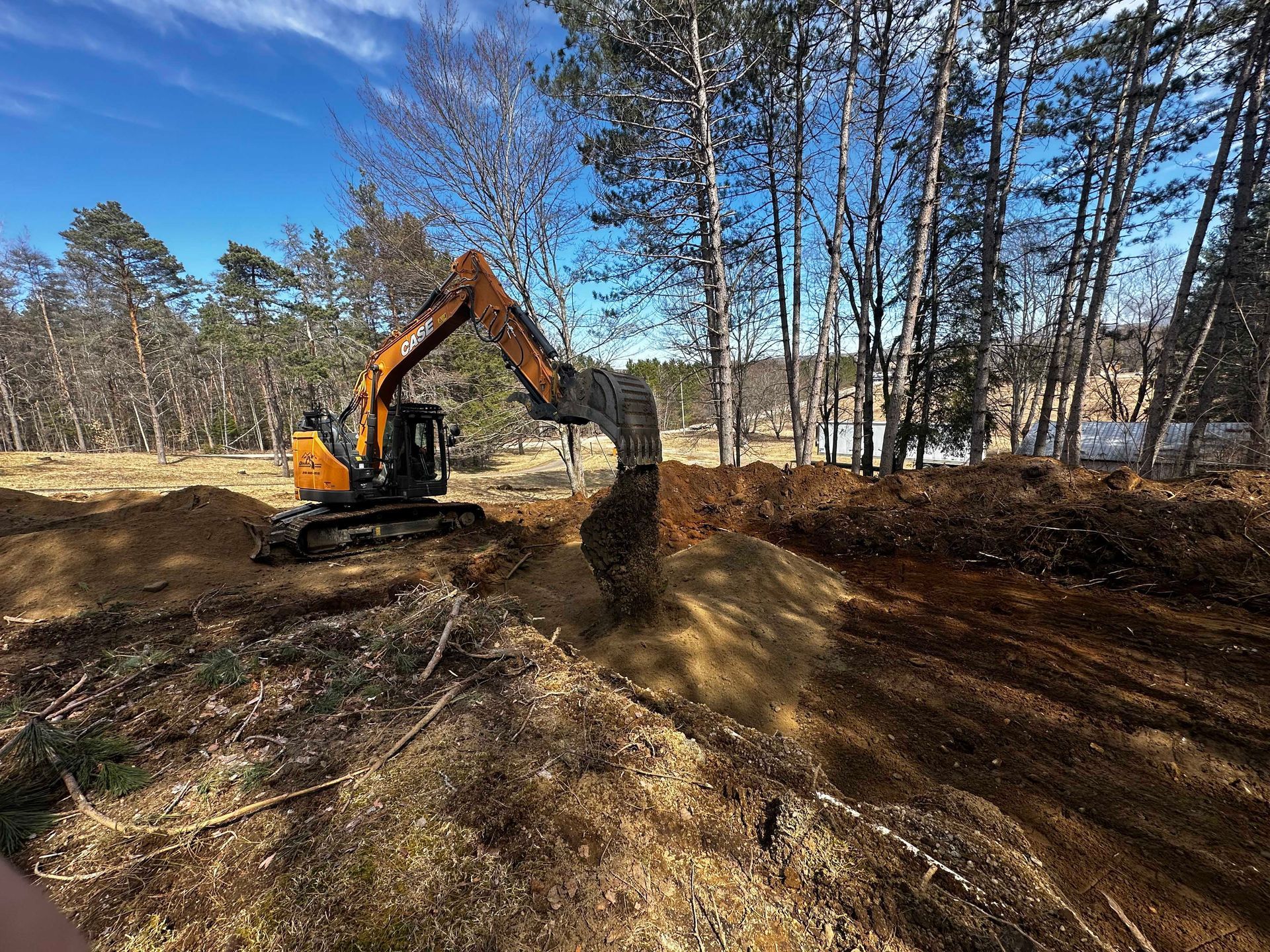 Une pelleteuse jaune creuse le sol dans une clairière entourée d'une forêt par une journée ensoleillée.