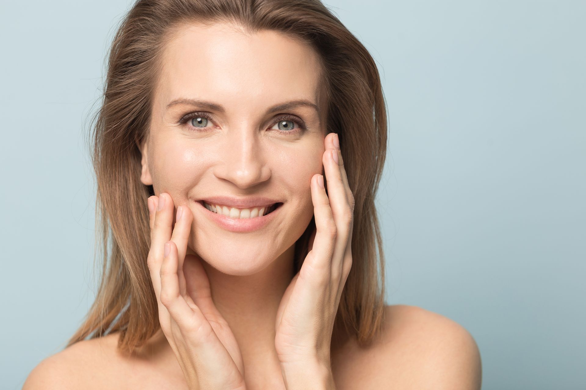 A woman is smiling and touching her face with her hands.