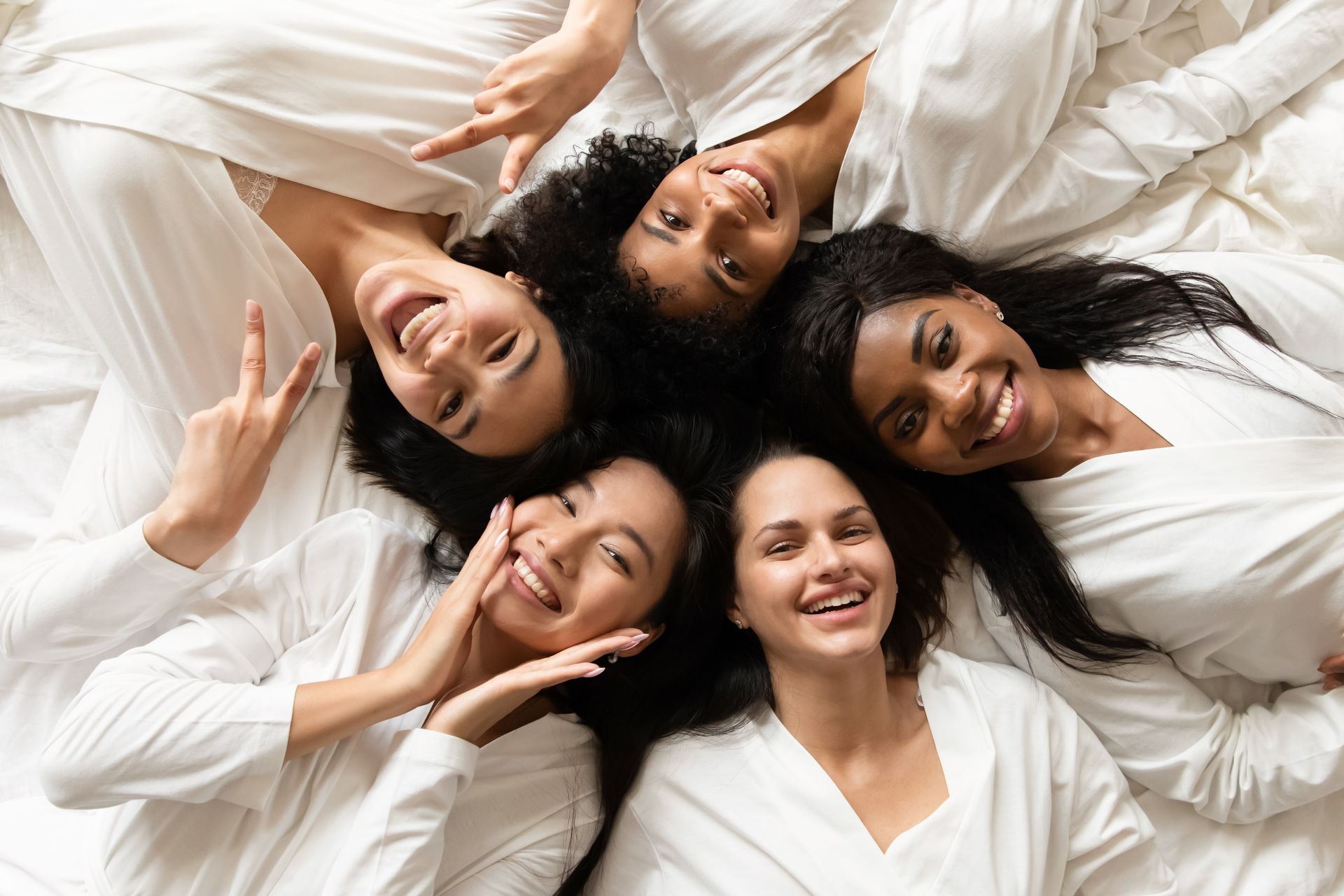 A group of women are laying in a circle on a bed and smiling.